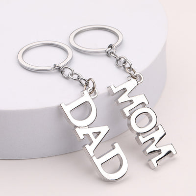 Two shiny silver-tone keychains with DAD and MOM letter pendants on a white display.