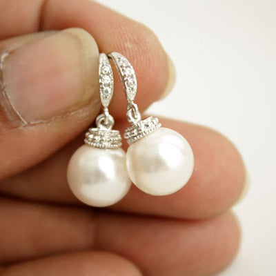 Silver faux pearl drop earrings held between fingers close-up