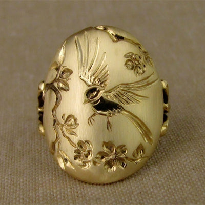 Front gold oval bird flower engraved face ring on beige fabric