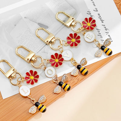 Gold-tone keychains spelling LOVE displayed together with red daisy and rhinestone bee charms