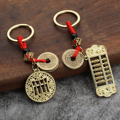 Two gold-tone abacus keychains with red cords and coin charms on a wooden surface.