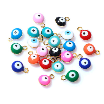 Overview of small round evil-eye discs in assorted enamel colors with gold-tone hanging loops arranged on a light backgr