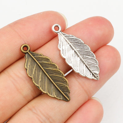 Assorted detailed leaf pendant charms in silver and bronze tones arranged together in the main product view