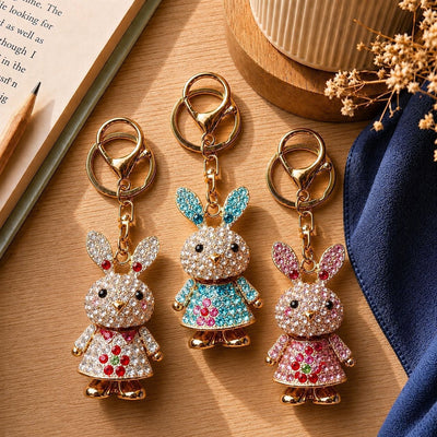 Three rhinestone rabbit dress keychains in white floral teal and pink on wood desk