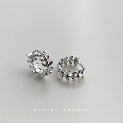 Silver olive leaf huggie hoops lying open on pale surface