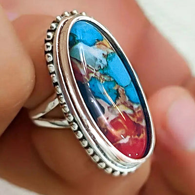 Close fingertip view of antique silver multicolor oval cabochon ring face