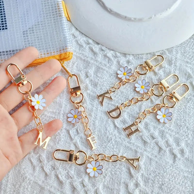 Hand holding several gold letter keychains with white daisy flowers and lobster clasps
