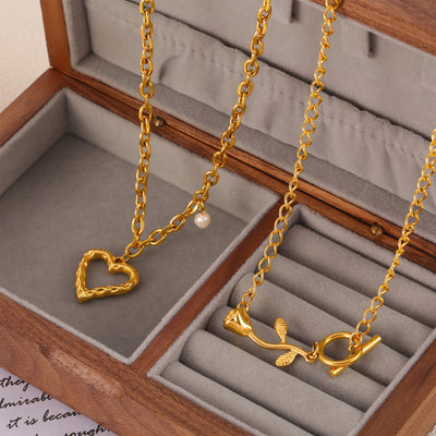 Two gold necklaces in a jewelry box: open heart with pearl and rose toggle