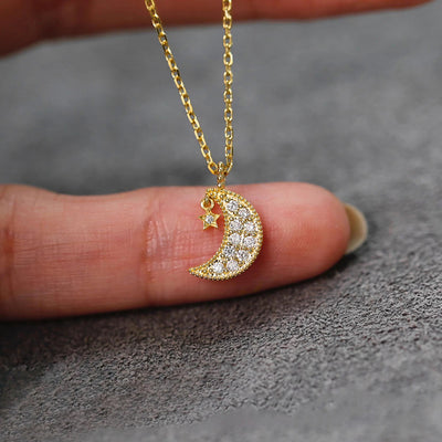 Gold crystal crescent moon star pendant held on a fingertip