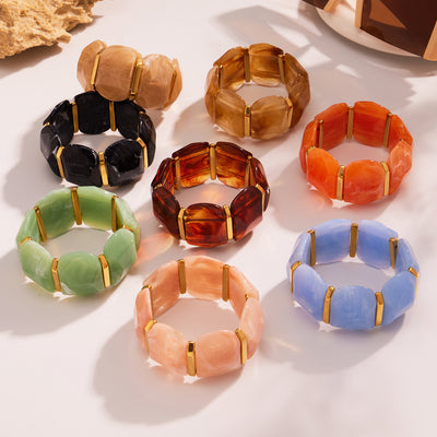 Nine multicolor wide resin stretch bracelets with gold spacers flat lay