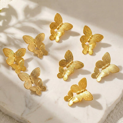 Multiple gold dual butterfly stud earrings scattered on marble