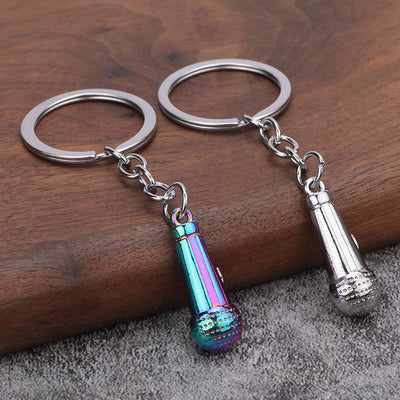 Two microphone-shaped keychains in silver and iridescent finishes rest on a wooden surface.