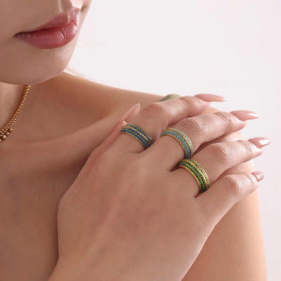Hand wearing three gold four-row pavé rings in turquoise and green
