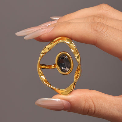 Hand holding gold irregular open frame ring with dark oval stone