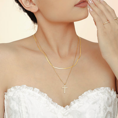 Model wearing layered gold snake chain and zircon cross pendant necklace