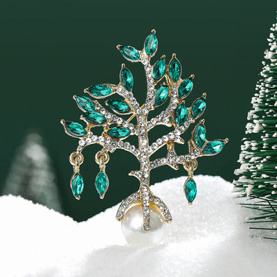 Display view of green crystal tree brooch with dangling stones and pearl-like drop standing on white blocks.