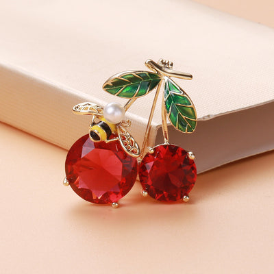 Red crystal cherry bee brooch resting against peach fabric book