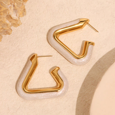 Pair of gold triangle hoops with pearl pink shell on sand surface
