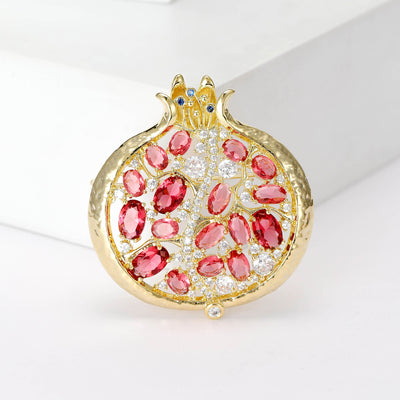 Gold pomegranate brooch with red crystals on white block