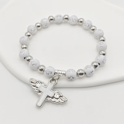 White cross bead stretch bracelet with winged cross on white dish