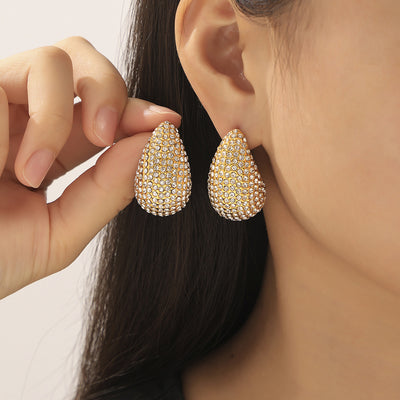 Model holding gold pave teardrop stud earring beside ear