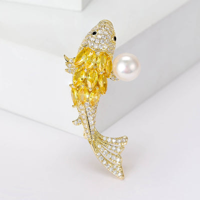 Front view of yellow crystal koi fish brooch with pearl against a white background.