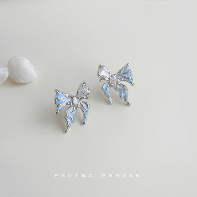 Silver blue liquid butterfly studs on pale surface with pebbles