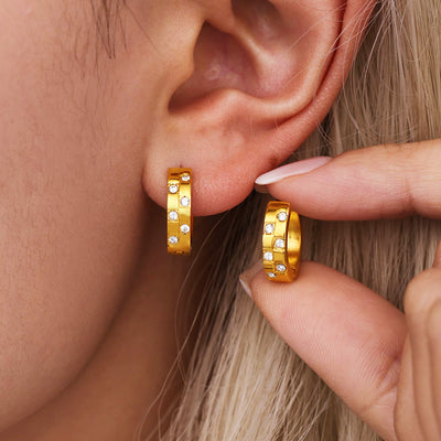 Model ear with gold geometric zircon huggie and matching hoop held nearby