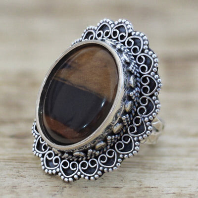 Angled front of antique silver filigree brown oval stone ring on wood grain