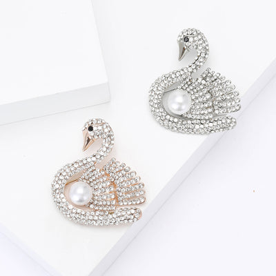 A crystal-covered swan curled around a round pearl-like accent shown on a white background