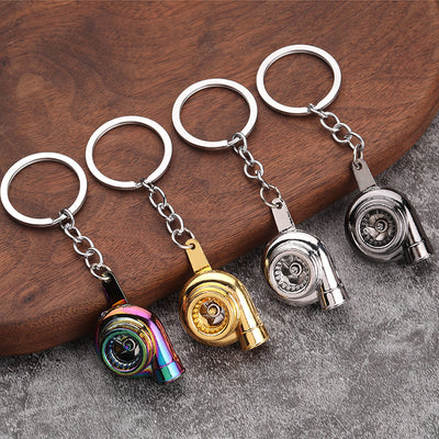 Four turbocharger-shaped keychains in rainbow, gold, silver, and dark silver finishes on wood and gray fabric.