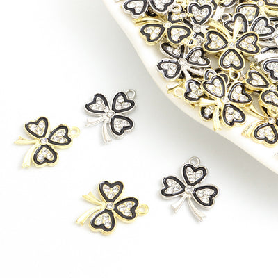 Assorted black outline four leaf clover charms arranged beside a tray on white