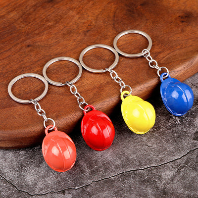 Four helmet keychains in orange, red, yellow, and blue rest beside a wooden board.