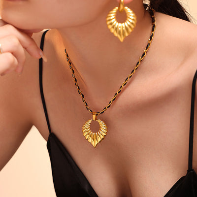Model wearing gold ribbed open-heart pendant on black-gold twisted cord necklace