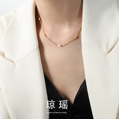 Gold curb chain pearl barrel necklace worn with cream blazer and black top