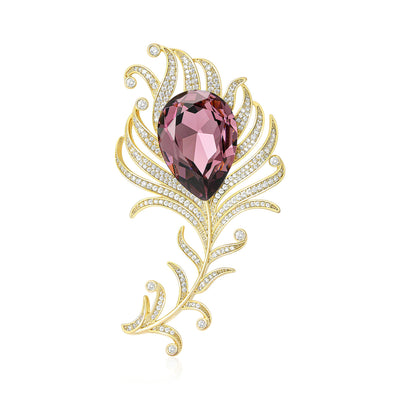 Front view of gold tone feather brooch with large purple teardrop crystal against a white background.