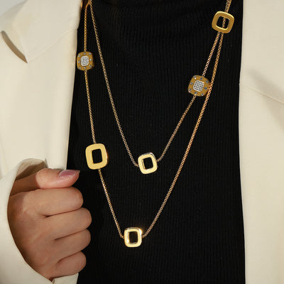 Model wearing long gold dual-layer necklace with square and crystal stations