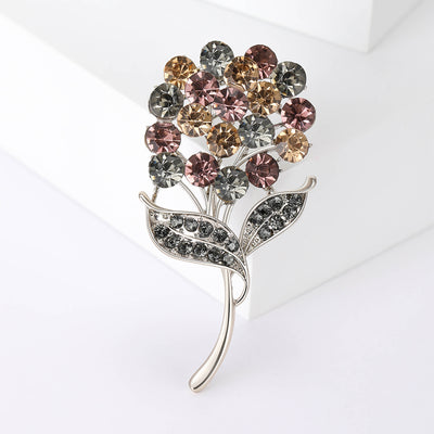 Front view of round crystal bouquet brooch with two gray stone leaves against a white background.