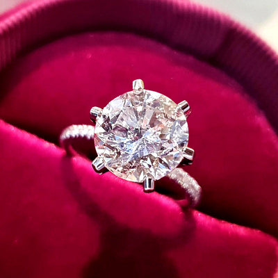 Silver six-prong round clear solitaire ring on red velvet pad