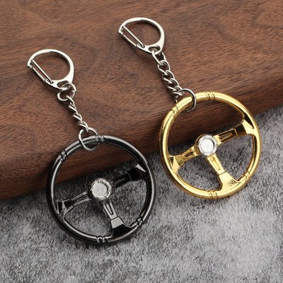Two steering wheel keychains in gunmetal black and gold beside a wooden surface.