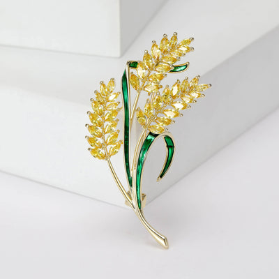 Front view of yellow crystal wheat brooch with three stalks and green leaves against a white background.