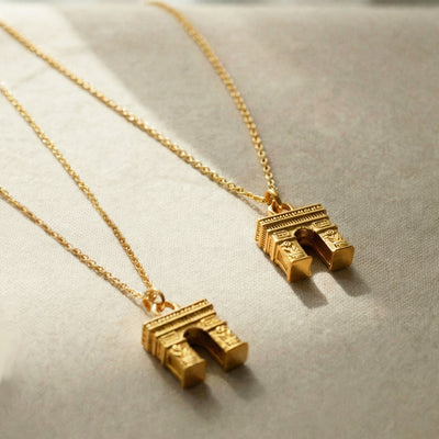 Two gold Arc de Triomphe pendants on chains resting on fabric