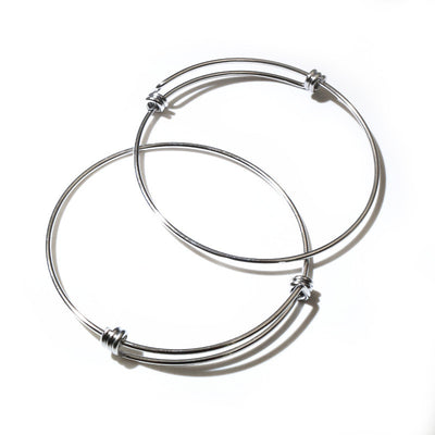 Overview of polished silver tone adjustable wire coil bangle bracelet arranged on white