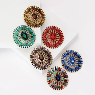 Front view of the oval radiating crystal brooch in six colors with polished metal detail on a white background