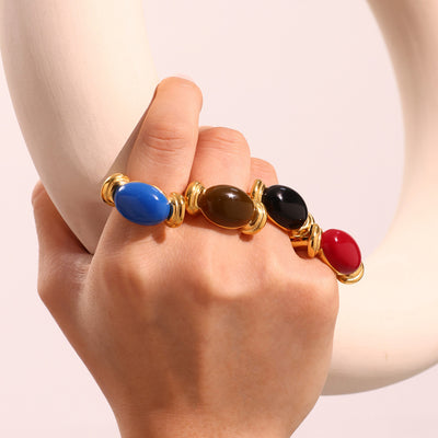 Hand wearing four gold oval resin open rings in blue brown black red