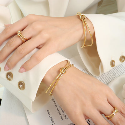 Hands wearing gold double-wire knot open bangles and matching knot rings