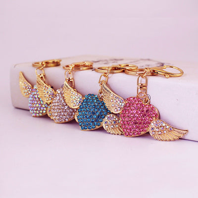 Four rhinestone winged heart keychains in pink, blue, white, and iridescent colors.