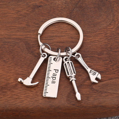 Silver-tone Papa keychain with hammer, screwdriver, wrench, and ruler-shaped tag on wood.