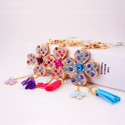 Three gold-tone four-leaf clover keychains shown in pink, blue and purple color styles.