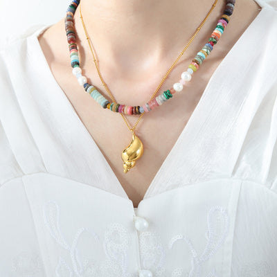Model in white blouse wearing gold conch pendant layered with multicolor beads